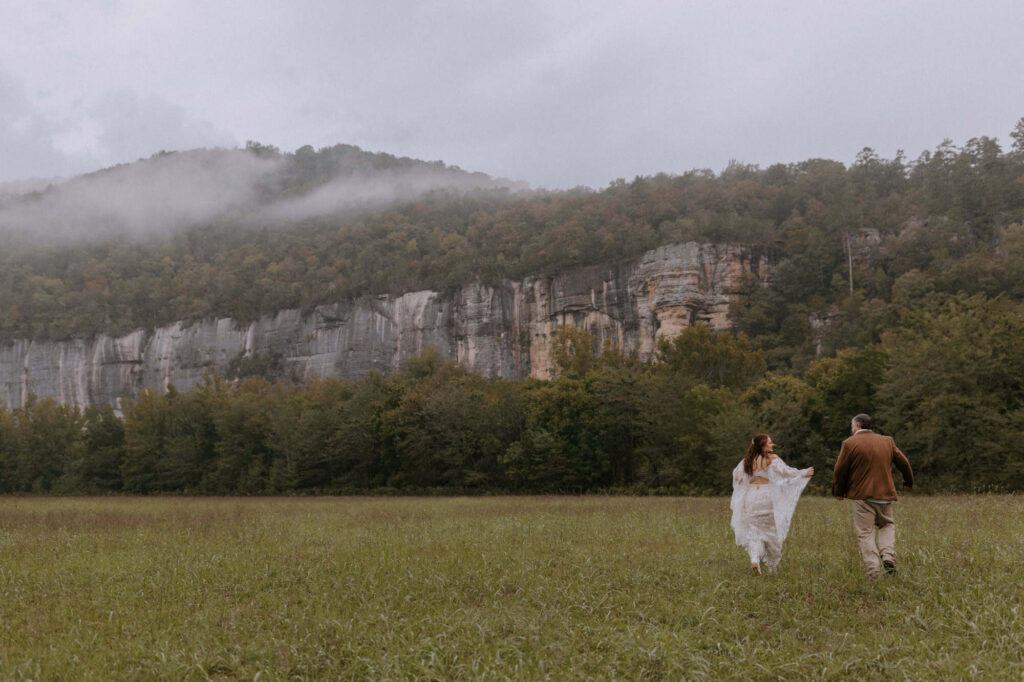 a couple runs through a field in front of Roark Bluff during their Buffalo National River elopement at Steel Creek.