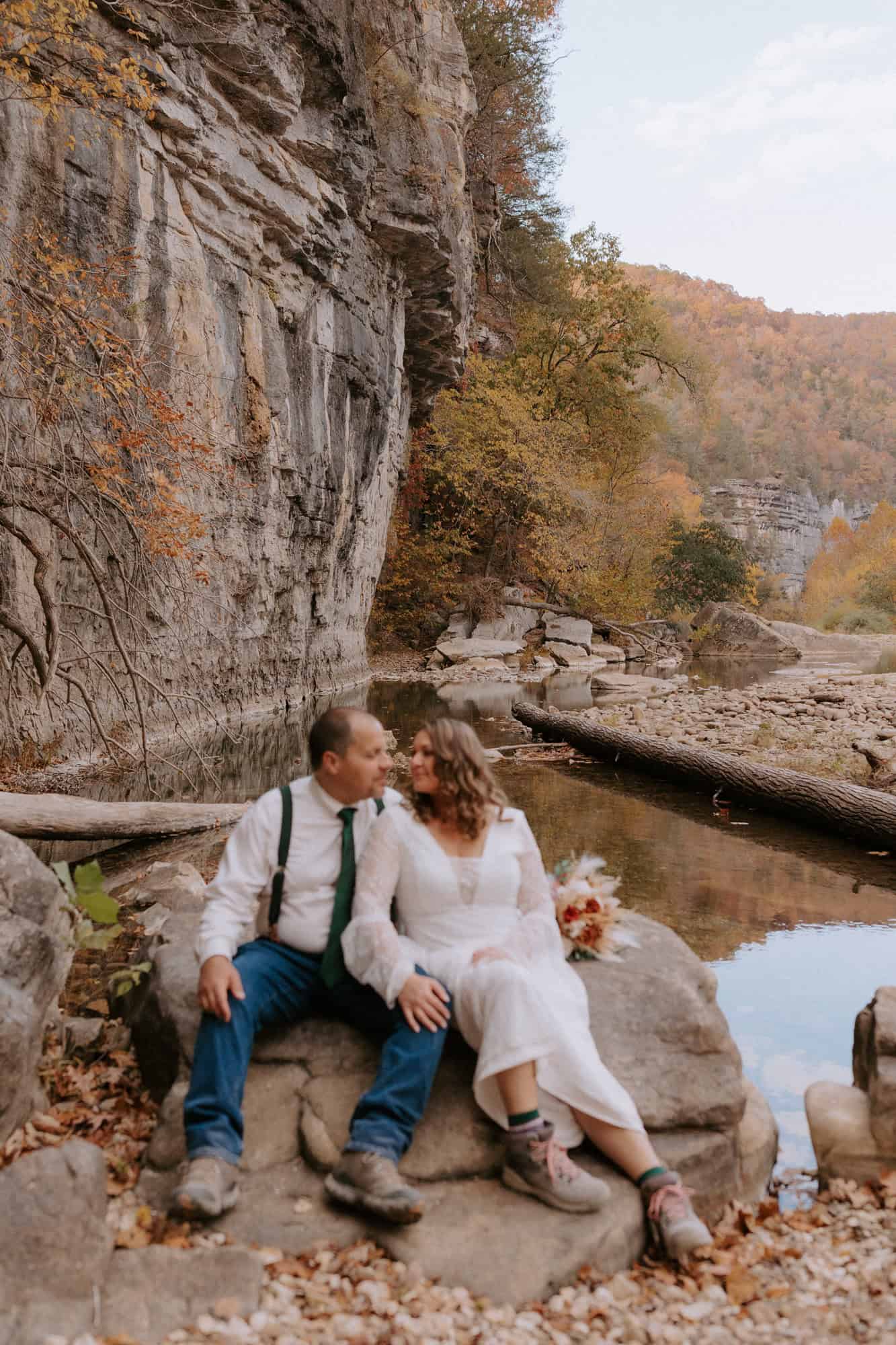 A couple sits on a rock in the dry river bed of the Buffalo National River during their Arkansas elopement at Steel Creek Campground.