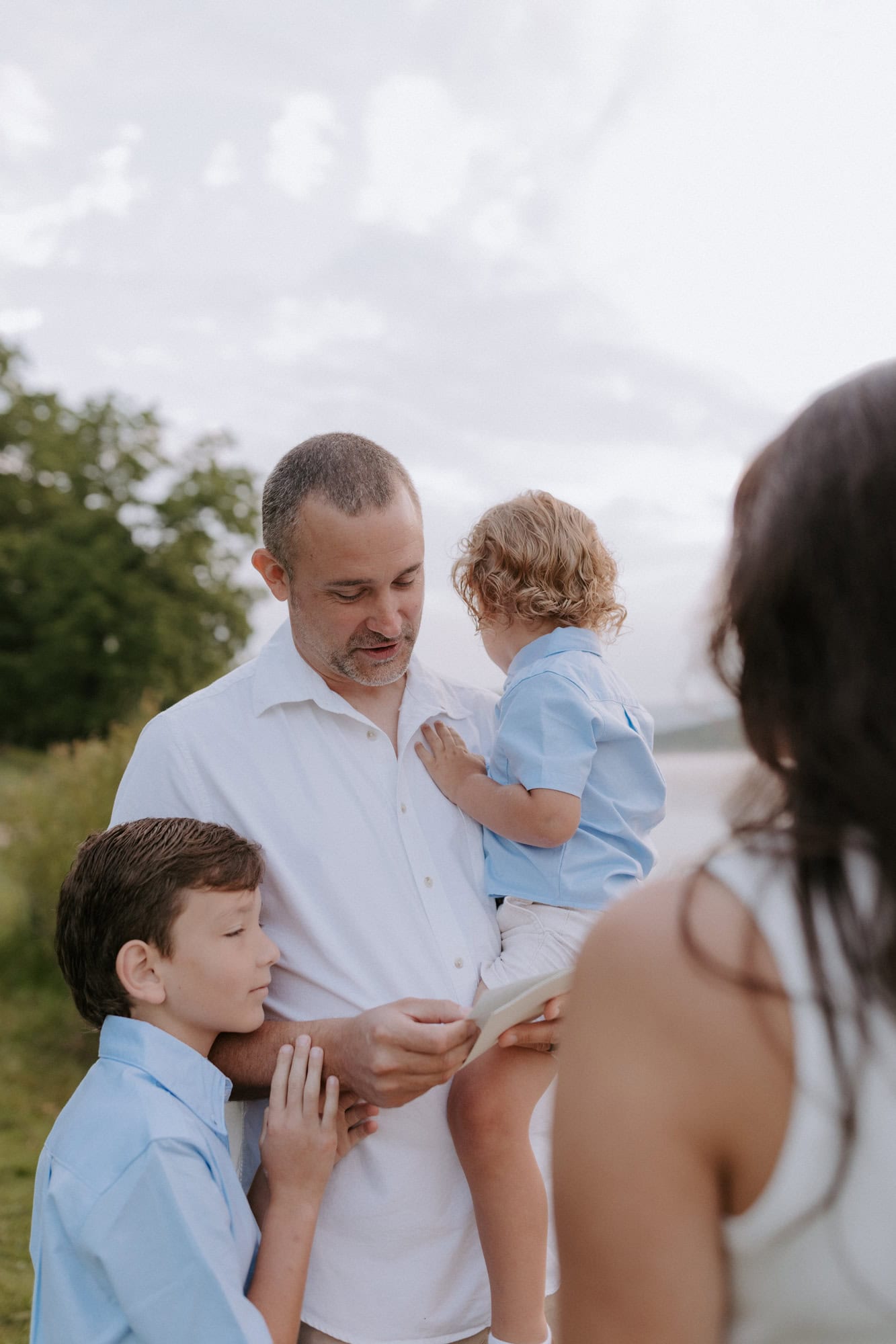 A husband holds on to his youngest child while his oldest holds on to his arm as he reads his vows to is wife on their 10th anniversary vow renewal in Eureka Springs, Arkansas.
