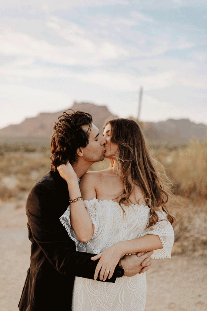 A couple in wedding attire embrace and kiss in front of the mountains and cacti of Phoenix, Arizona during their elopement.